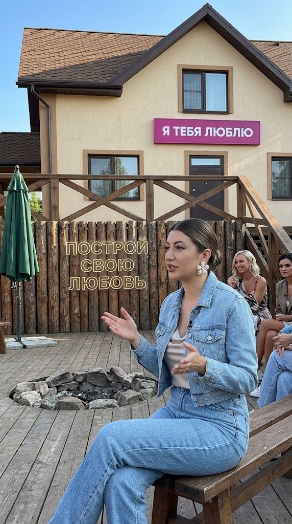 Создай эту женщину черты лица идентичной оригинала точь-в-точь как на фото исходники она сидит в красивом уличном джинсовом наряде А именно голубые толстые джинсы джинсовка короткая куртка и шелковый светлый топ у неё объемные красивые серьги в виде цветов из жемчужин красивый дневной макияж Волосы собранные назад у неё уложены волосы она о чем-то рассуждает жестикулируя сидя на лобном месте Телепередачи Дом 2 Позади светящиеся вывеска «Построй свою любовь »Рядом с ней сидит Ольга бузова И Май Солнцев И чуть подальше Ксения Бородина
Фон : запечатлевает уличную сцену с полукруглой деревянной баррикадой, построенной из вертикально расположенных бревен, каждое из которых имеет примерно цилиндрическую форму диаметром от 10 до 15 сантиметров. Бревна плотно расположены и имеют естественную шероховатую текстуру с остатками коры в выцветших серых и коричневых тонах, формируя вогнутую форму к зрителю. Поддерживающие горизонтальные балки и крупные диагональные бревна диаметром около 20-25 сантиметров укрепляют конструкцию под углом 45 градусов. На переднем плане средне-коричневые деревянные доски образуют настил с матовой отделкой, на котором видны едва заметные волокна. По центру на этом настиле расположена круглая композиция из светло-серых и бежевых камней диаметром около 40 сантиметров. За баррикадой находится двухэтажное здание с крутой крышей, покрытой коричнечной асфальтовой черепицей, со светло-бежевыми стенами и прямоугольными окнами в темной рамке. Над ними вывешена магента вывеска с белым кириллическим текстом «Я ТЕБЯ ЛЮБЛЮ». Слева от баррикады стоит закрытый зеленый патийный зонт, а справа видна наклонная деревянная конструкция. Естественный дневной свет отбрасывает мягкие тени, подчеркивая текстуры на фоне ясного синего неба.